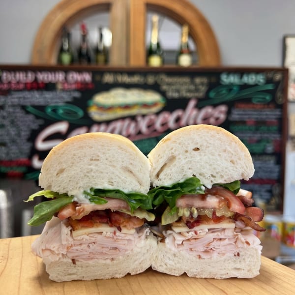 A turkey and bacon sandwich, cut in half, on a wooden board with a menu in the background.