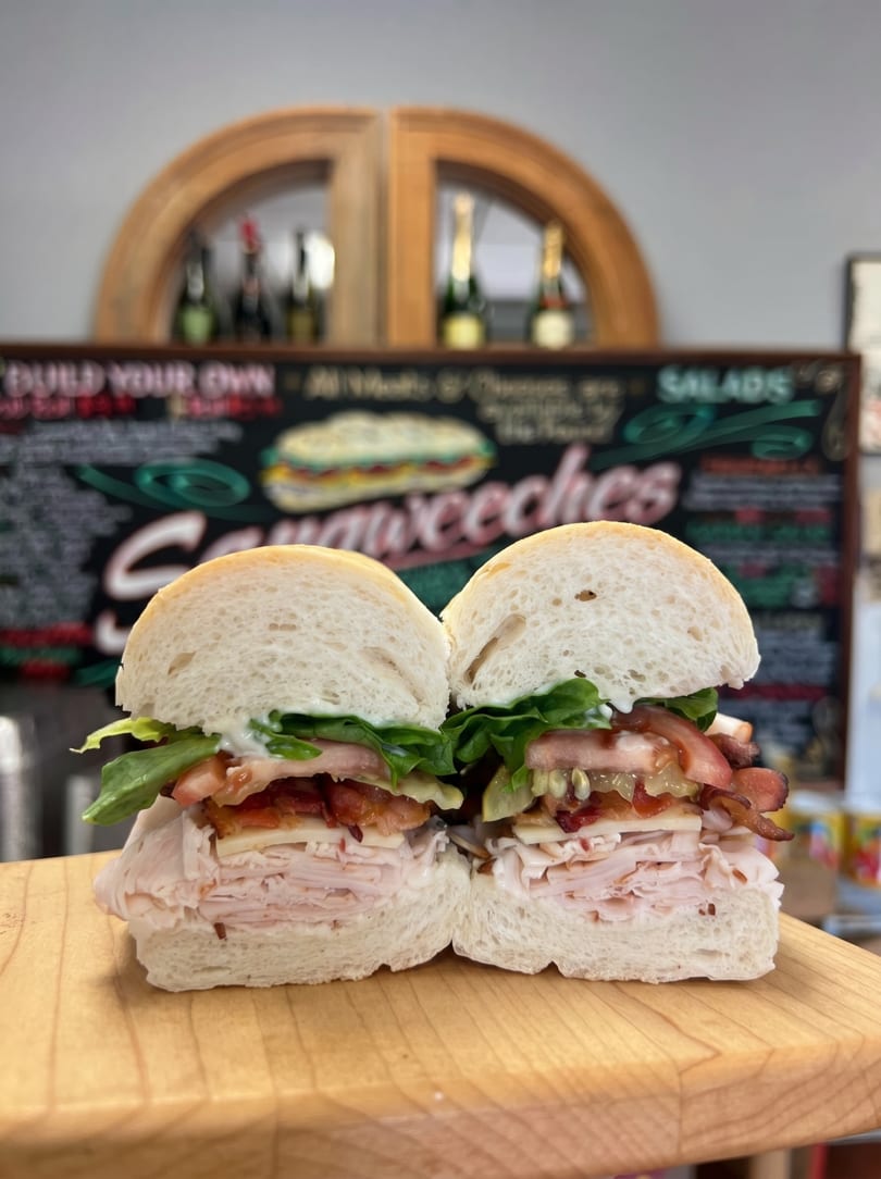 A turkey and bacon sandwich, cut in half, on a wooden board with a menu in the background.
